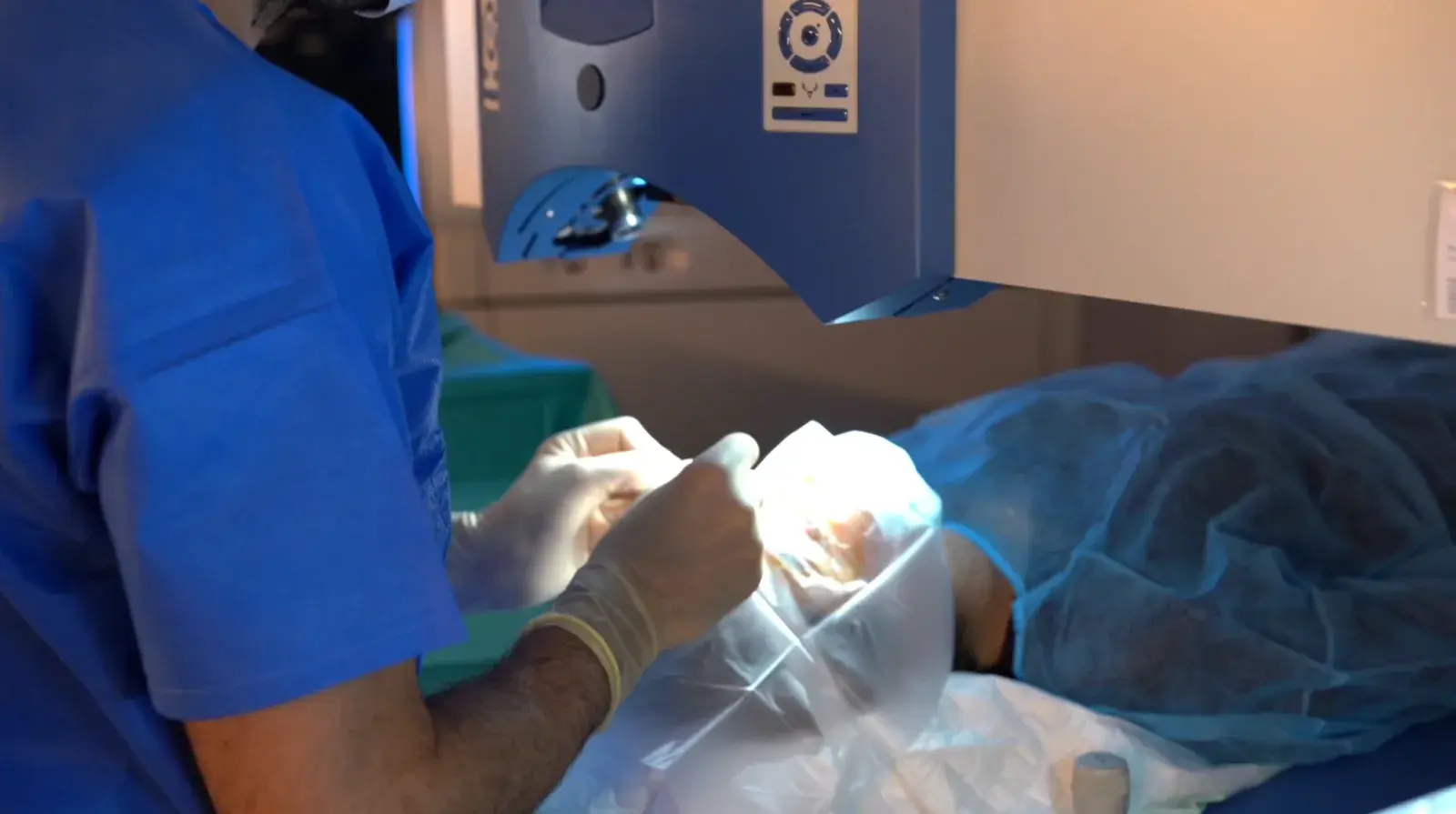 Les mains gantées du chirurgien préparent l'œil du patient sous le laser.