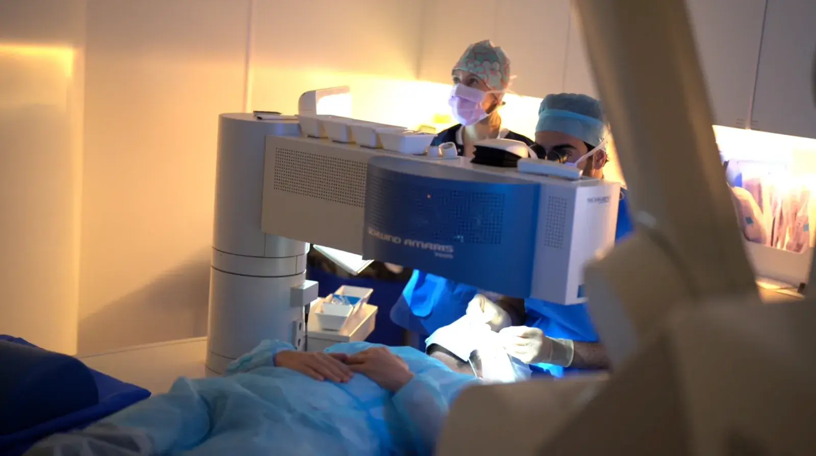 Une salle de chirurgie réfractive : la patiente est allongée sous le laser, deux membres de l'équipe opèrent.