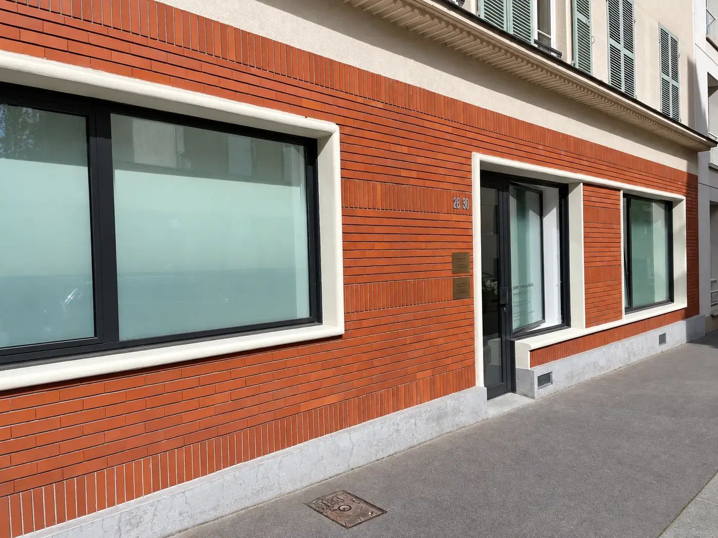 L'entrée du cabinet vue du trottoir, avec le numéro de la rue et les plaques des praticiens à côté de la porte.